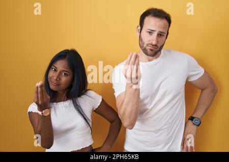 Interracial couple standing over yellow background doing italian gesture with hand and fingers confident expression Stock Photo