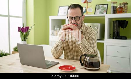 Middle age man using laptop drinking coffee at home Stock Photo