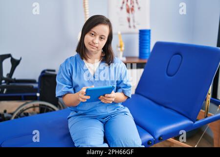 Down syndrome woman wearing physiotherapy uniform using touchpad at physiotherapist clinic Stock Photo