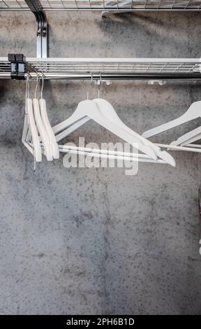 White clothes hangers on a rack with concrete wall behind Stock Photo