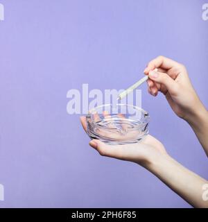 Female hands with natural nails hold a joint with medical marijuana and an empty glass ashtray on a light purple background.  copy space Stock Photo
