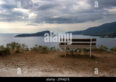 Early morning at a hill on the south of the island. Wooden empty bench with a view on the Thracian sea, little island and peninsula. Cloudy sky. Thass Stock Photo