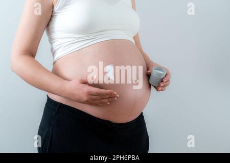 Pregnant woman applying white cream on the belly taking care of skin Stock Photo