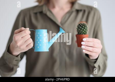 Woman holds blue watering can and spiked cactus in pot Stock Photo