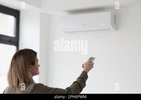 Woman uses remote control to adjust air conditioner Stock Photo
