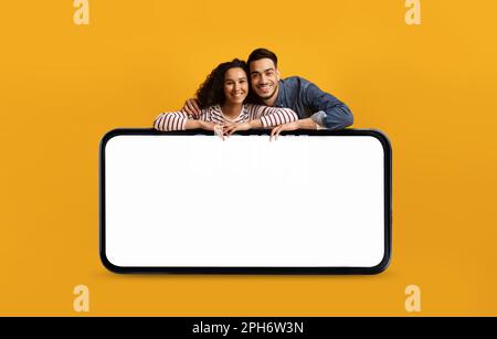 Happy Arab Couple Leaning At Big Smartphone With Blank White Screen Stock Photo