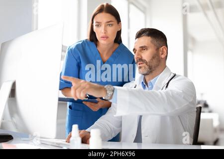 Male and female doctors team discussing patient diagnosis data, using computer in office clinic, working together Stock Photo