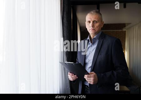 Portrait of a businessman who stands and holds documents in his hands, looks at the camera. Stock Photo