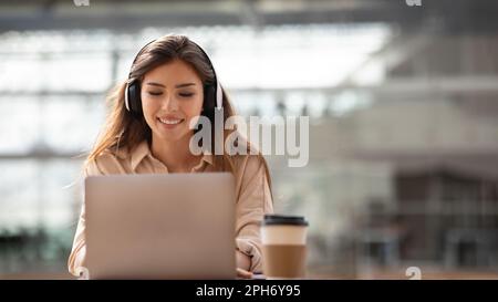 Happy young european woman student in wireless headphones works at laptop, study at university Stock Photo