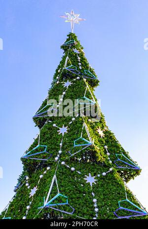 Large plastic decorated Christmas tree with balls against the blue sky background. New Year's celebration Stock Photo