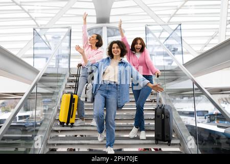 Travelling Together. Three Cheerful Women With Suitcases Having Fun At Airport Stock Photo