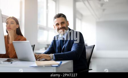 Businessman and businesswoman working at computer and laptop in office, man looking aside at free space, panorama Stock Photo