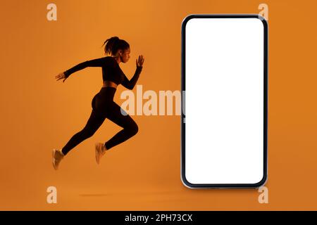 Workout application. Fit african american lady exercising near big cellphone over neon orange background, mockup Stock Photo