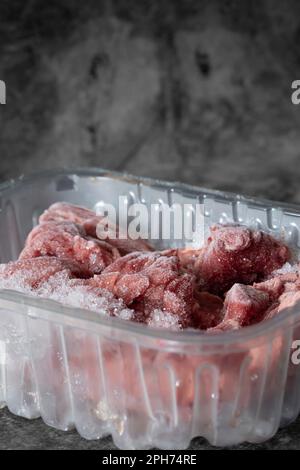 Frozen lean beef steak cubes in clear plastic tray packaging. On a dark stone background Stock Photo