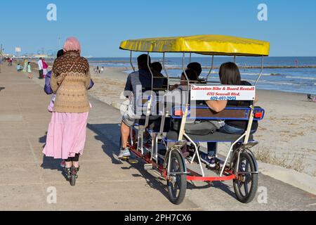 Galveston, Texas, USA - February 2023: People on an electric scooter riding alongide people in a pedal cart on the city's promenade Stock Photo