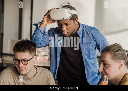 IT Development Team Working on VR Project. Man wearing VR headset, playing and touching something in the virtual world. Diverse men programmers using Stock Photo