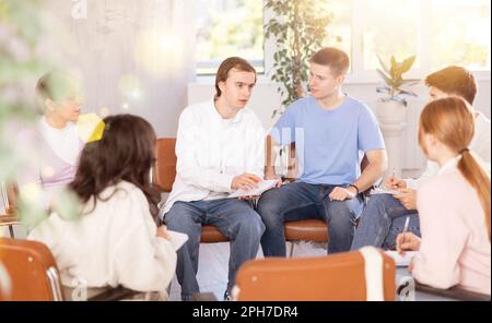 Cheerful young student discussing learning assignment with coursemates Stock Photo
