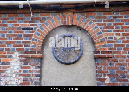 A rusty old clock face under a brick arch Stock Photo