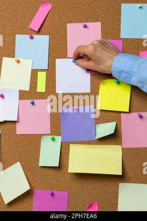 A hand holds a blank sticker for writing ideas on a cork board. Stock Photo