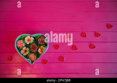 On pink wooden background lies box of edible marshmallow flowers, in the shape of heart with red candles. Top view, still life, flat lay. Sweet gift f Stock Photo
