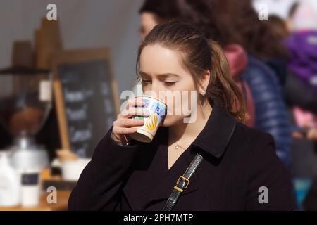 A young woman enjoys freshly brewed coffee from an Easter-themed cup at a farmers market in Prague Stock Photo