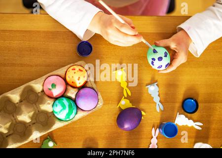 Childs hands painting eggs for Easter on the wooden table at home. Preparation for happy Easter. Stock Photo