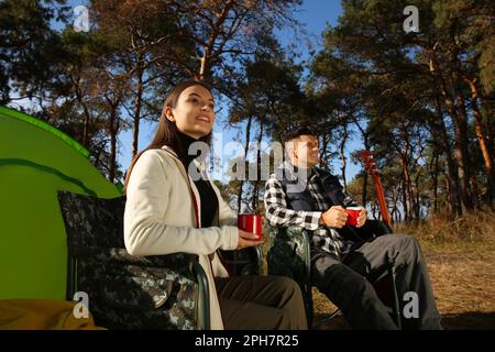 Couple resting in camping chairs and enjoying hot drink outdoors Stock Photo