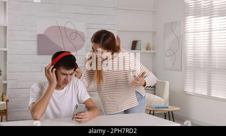 Teenage son listening music in headphones or playing online games ignoring  his mother Stock Photo - Alamy