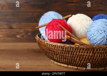 Wicker basket with clews of colorful knitting threads and crochet hooks on wooden table, closeup. Space for text Stock Photo