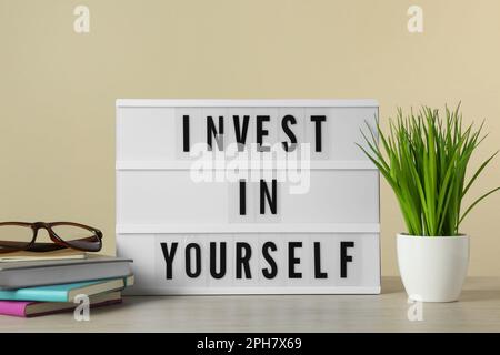 Lightbox with motivational quote Invest in Yourself, stationery and plant on white wooden table Stock Photo