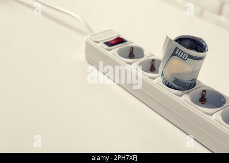 Extension board with rolled dollar banknotes on white table, closeup Stock Photo