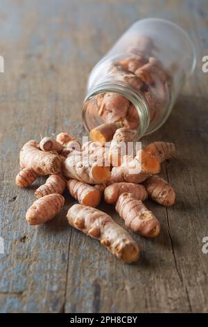 cleaned turmeric rhizomes or roots scattered on table top with a glass bottle, curcuma longa, commonly used spice in cooking and medicine Stock Photo