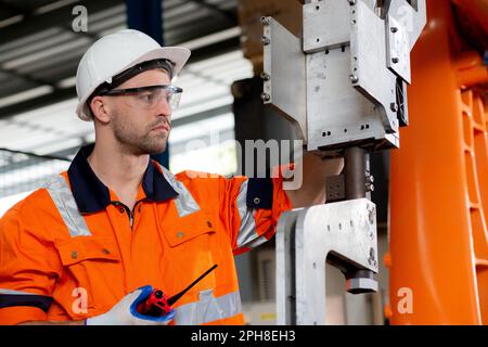 Young caucasian engineer man inspection robot arms technology intelligence and innovation while speak radio command at factory, technician check and m Stock Photo