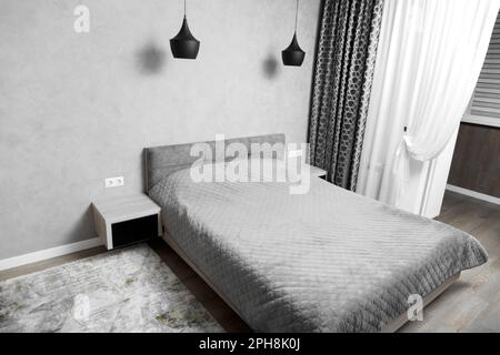 Modern design of the bedroom in gray tones, minimalism in the interior. A large bed in the bedroom, bedside tables with black glass, black chandeliers Stock Photo