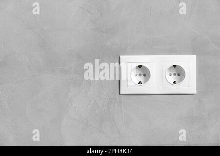 Plastic white double electrical socket on gray texture wall close-up with space for text. Stock Photo