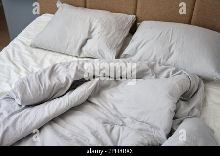 Unmade bed after sleeping. Crumpled bed with pillows, blanket and crumpled sheets in bedroom. Morning housekeeping Stock Photo