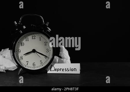 Depression sign, alarm clock and used tissues on black table against dark background, space for text Stock Photo