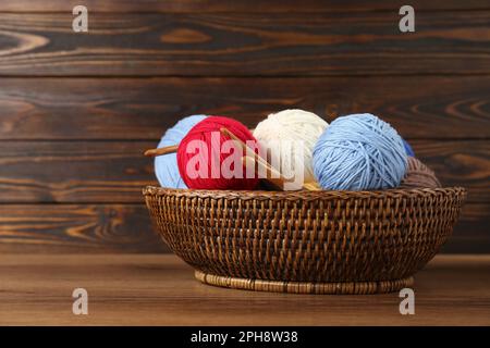 Wicker basket with clews of colorful knitting threads and crochet hooks on wooden table Stock Photo