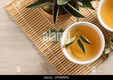 Aromatic sage tea and fresh leaves on wooden table, flat lay. Space for text Stock Photo