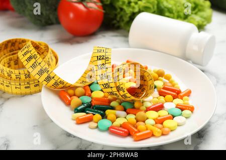 Plate with different weight loss pills and measuring tape on white marble table Stock Photo
