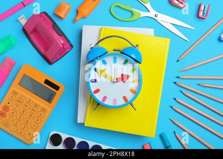 Flat lay composition with alarm clock and different stationery on light blue background. School time Stock Photo