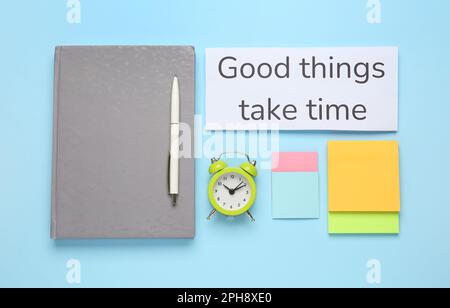 Different stationery, alarm clock and card with motivational quote Good Things Take Time on light blue background, flat lay Stock Photo