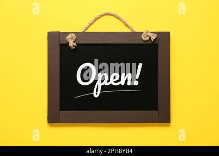 Small chalk board with word Open on yellow background Stock Photo