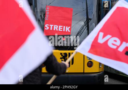 Dresden, Germany. 27th Mar, 2023. Employees of the Dresdner Verkehrsbetriebe (DVB) stand with Verdi flags in front of streetcars during the warning strike at the Trachenberge depot. With a large-scale nationwide warning strike, the unions EVG and Verdi have paralyzed large parts of public transport on Monday. Credit: Robert Michael/dpa/Alamy Live News Stock Photo