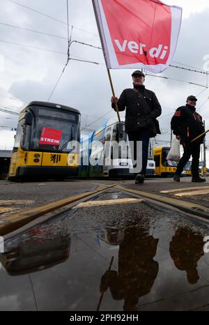 Dresden, Germany. 27th Mar, 2023. Employees of the Dresdner Verkehrsbetriebe (DVB) stand with Verdi flags in front of streetcars during the warning strike at the Trachenberge depot. With a large-scale nationwide warning strike, the unions EVG and Verdi have paralyzed large parts of public transport on Monday. Credit: Robert Michael/dpa/Alamy Live News Stock Photo