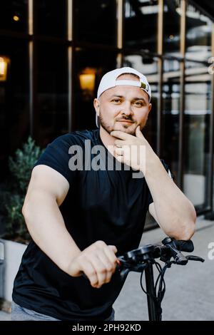 Pleasant smiling man riding a kick scooter. Happy man riding kick scooter Stock Photo