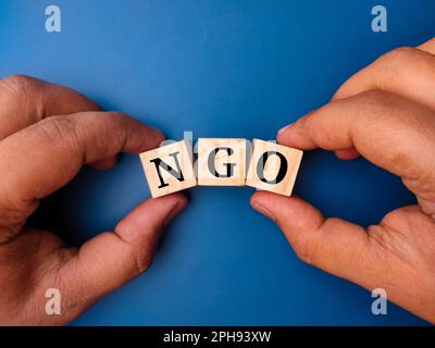 Hand holding colored cube with the word NGO on blue background Stock Photo