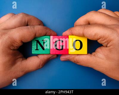 Hand holding colored cube with the word NGO on blue background Stock Photo