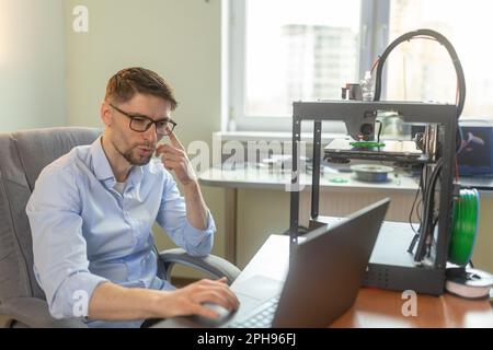 Engineering student working in the lab with a laptop, 3D printer in the background Stock Photo