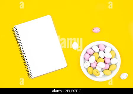 Colored Easter eggs and a blank notepad on a yellow background. Stock Photo